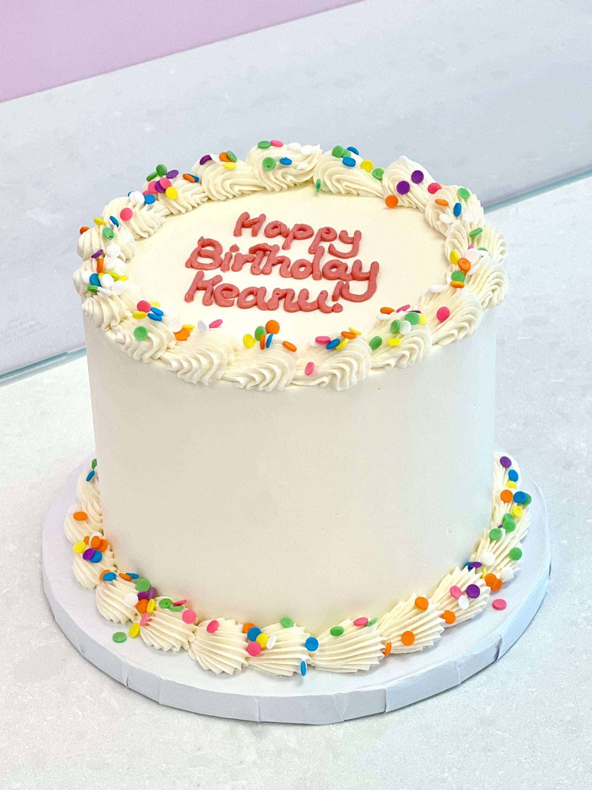 White birthday cake with colorful sprinkles and 'Happy Birthday Reenie' text on a white surface.