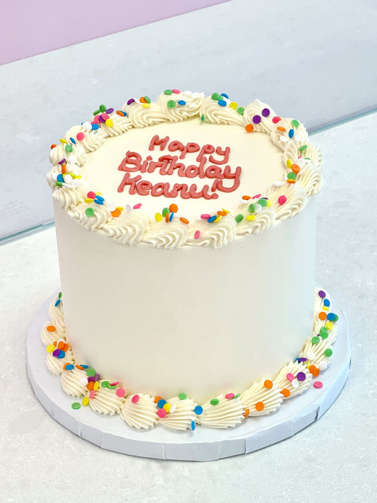 White birthday cake with colorful sprinkles and 'Happy Birthday Reenie' text on a white surface.