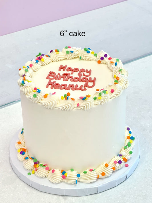 Small birthday cake with colorful sprinkles and 'Happy Birthday' text on a white surface.